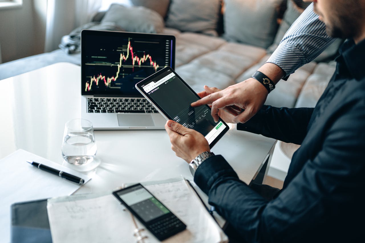 Professionals reviewing stock market trends on a tablet and laptop, discussing investment strategies.