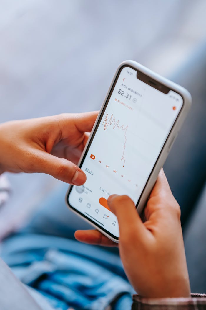 From above of crop anonymous person using smartphone and checking financial information against blurred background in daytime